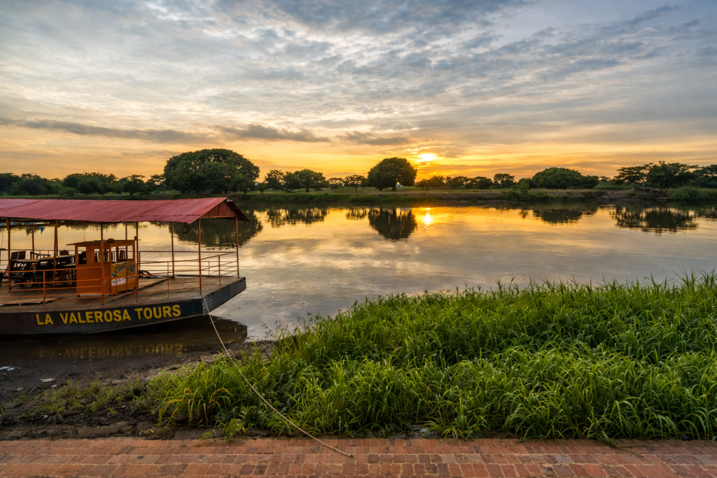 Illustration réaliste du fleuve Magdalena à Mompox au coucher du soleil, avec bateau traditionnel et paysage naturel en Colombie